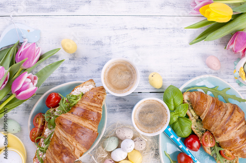 Breakfast for two. Croissants with salad and espresso. Fresh juice and sweets. Spring tulips. Easter decor. White wooden background.
