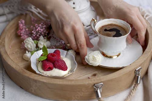 Morning coffee in bed and oat flakes with raspberry berries. Vintage ceramics. Decor of flowers. Breakfast on the wooden tray. Female hands. Good morning