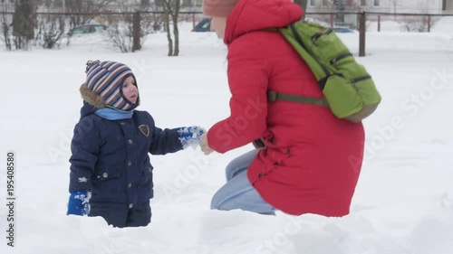 Cute little boy and young mother play in the winter with snow in the park. Blue kid's jacket and red at mom.
