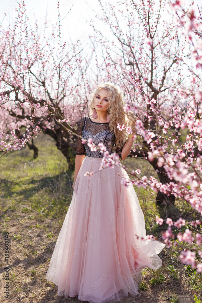 Beautiful woman in a long dress, in the garden of blooming peaches