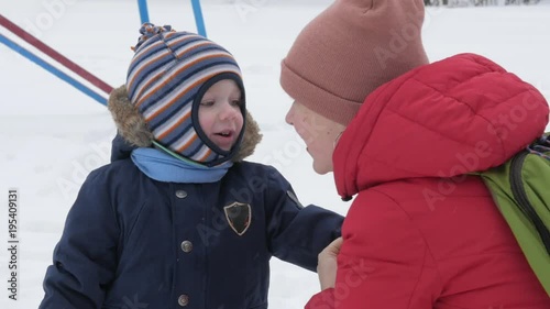Cute little boy and young mother play in the winter with snow in the park. Blue kid's jacket and red at mom.