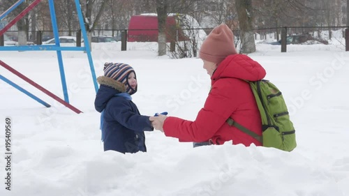 Cute little boy and young mother play in the winter with snow in the park. Blue kid's jacket and red at mom.