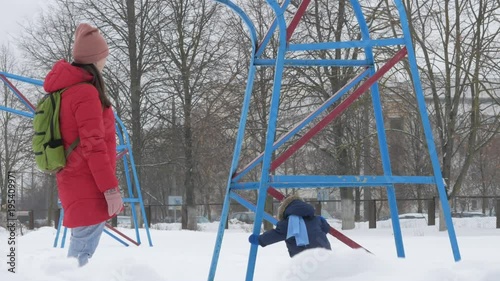 Cute little boy and young mother play in the winter with snow in the park. Blue kid's jacket and red at mom.