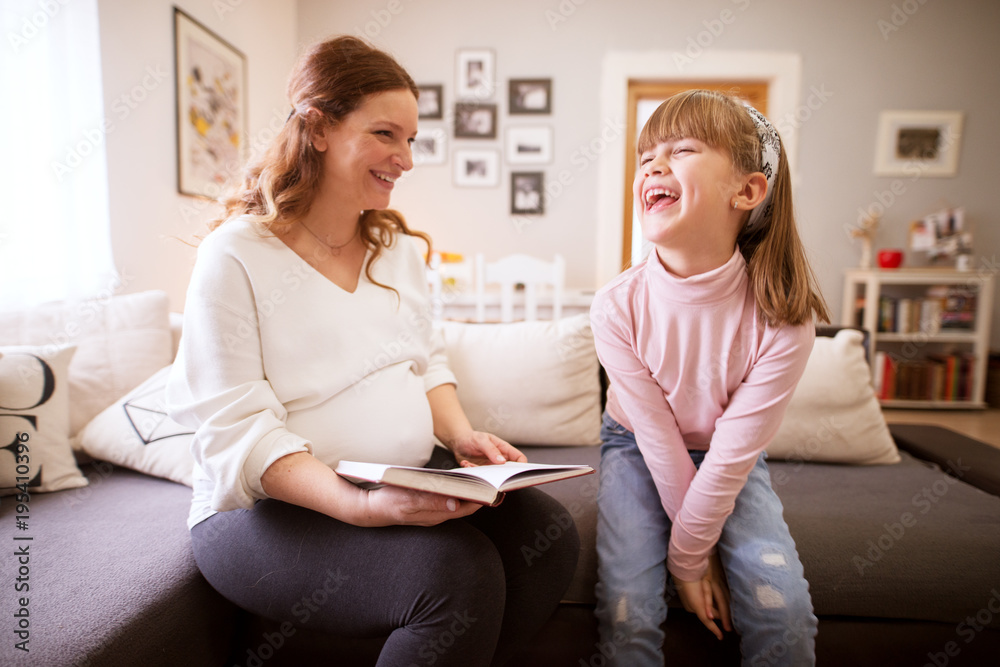 Cute cheerful smiling toddler girl laughing while her pregnant mum reading story. Cute cheerful smiling toddler girl laughing while her pregnant mum reading story.