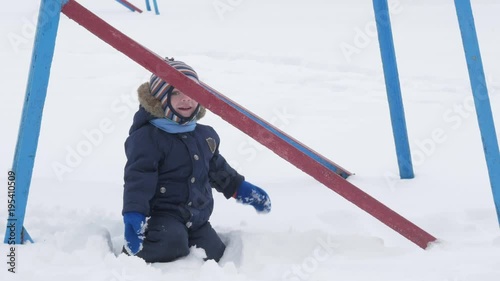 Cute little boy and young mother play in the winter with snow in the park. Blue kid's jacket and red at mom.