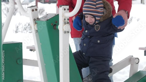 A cute little boy and a young mother are engaged in outdoor exercise equipment. It's hard for a kid to reach the handles of equipment