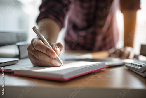 Hand of businessmen holding pen while writing notes in the book during the meeting.. © xreflex