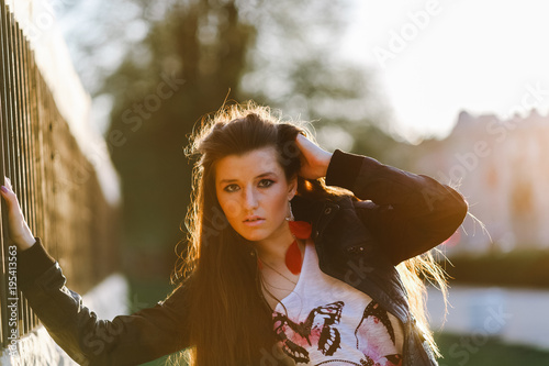 Fashion woman in casual clothes and a black leather jacket on the urban background of the city portrait. Fashion model with long hair posing on street at sunset. An elegant look to a lady. Toned photo photo