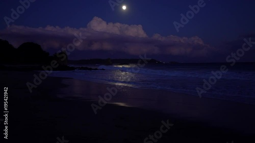 Full moon rising behind clouds at night beach