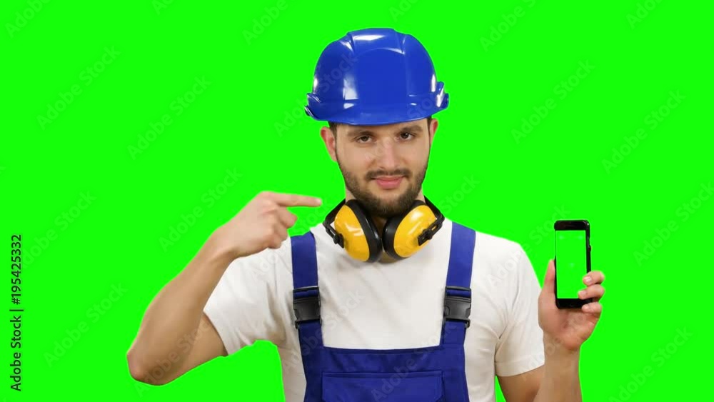 Man in a builder's suit advertises a smartphone. Green screen. Mock up Man in a builder's suit advertises a smartphone. Green screen. Mock up