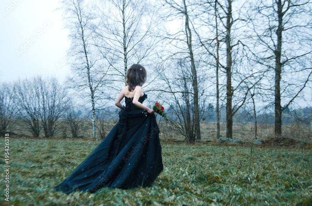 woman in a black wedding dress is on the edge of a flown autumn forest and looks out for someone in the distance