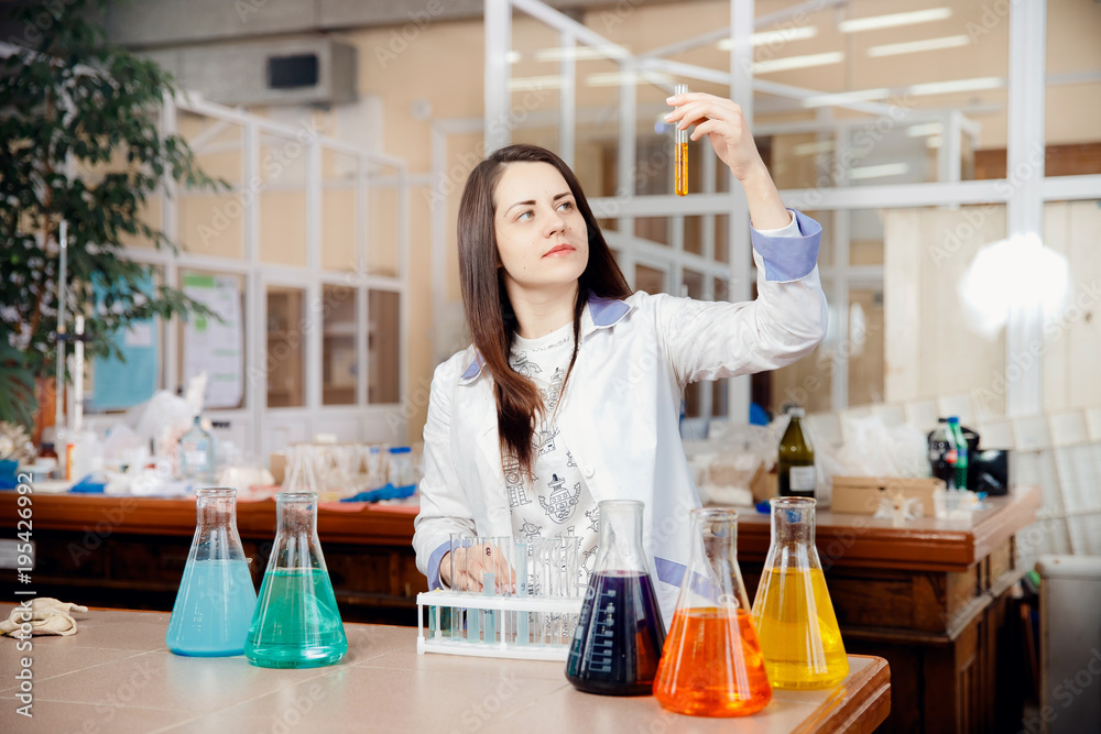 Close-up of a young woman in a white coat looks at the flasks with liquid. Concept student of the Faculty of Chemistry. Close-up of a young woman in a white coat looks at the flasks with liquid. Concept student of the Faculty of Chemistry.