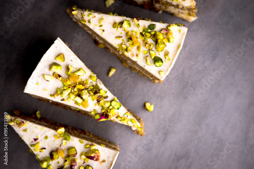 Raw vegan pistachio carrot cake with cashew cream layers from above on concrete table. Dark food photography styling concept.