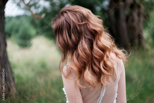 young pretty bride with curls n white wedding dress outdoors, view from behind