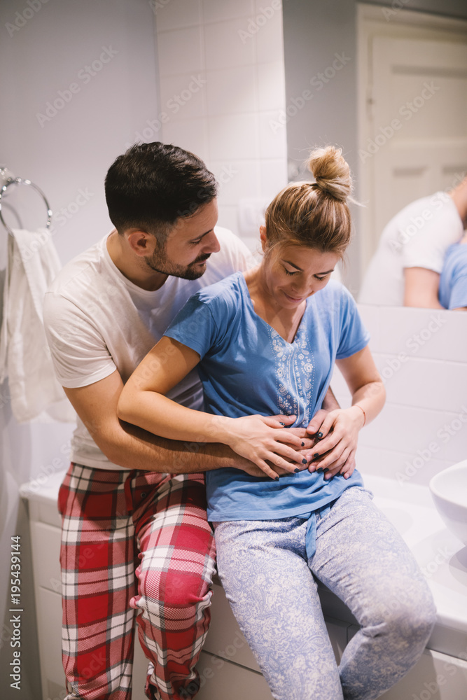 Happy beautiful couple in the bathroom in pajamas hugging together girls stomach while waiting for a baby. Happy beautiful couple in the bathroom in pajamas hugging together girls stomach while waiting for a baby.