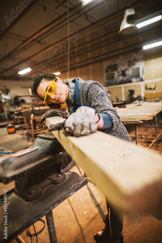 Obraz na plátně Portrait view of happy attractive hardworking middle aged professional female carpenter worker looking and choosing wood in the workshop or garage