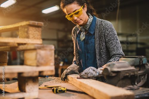 Portrait view of happy attractive hardworking middle aged professional female carpenter worker looking and choosing wood in the workshop or garage.