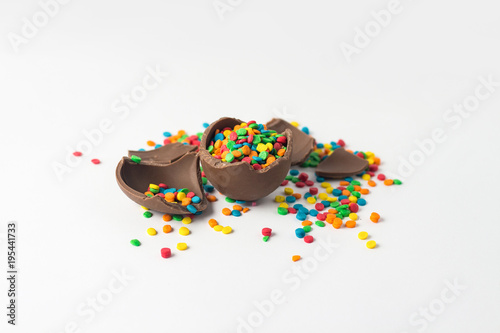 Broken Chocolate Easter egg with multi-colored candy decorations on a white background. Easter concept