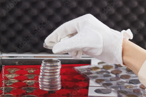 Fotografía Hand in the glove holds collector coin in the boxes
