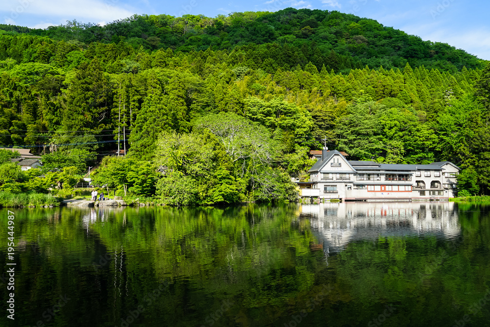 Beautiful abundant natural shades of green mountain background reflection on fresh lake Kinrinko with buildings in springtime, Yufuin