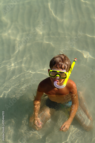 A boy in a swimming mask sits in the water