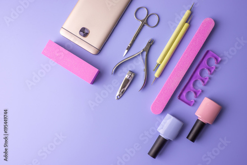 Set of cosmetic tools for manicure and pedicure on a purple background. Gel polishes, nail files and clippers, top view