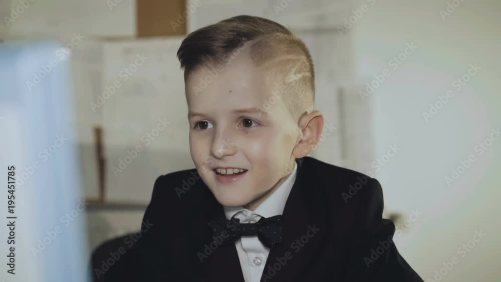 Little joyful boy in suit plays computer game and wins in office. 4K