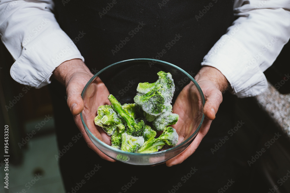 Man of 59 year old  shows frozen broccoli in the kitchen of his house.