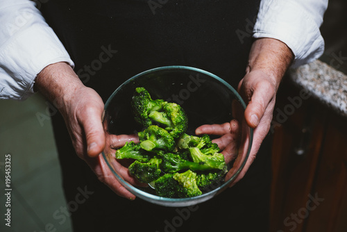 Man of 59 year old  shows  broccoli in the kitchen of his house.