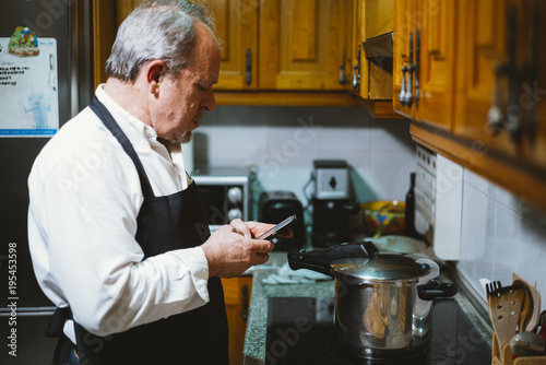 Man of 59 year old with smartphone in the kitchen of his house.