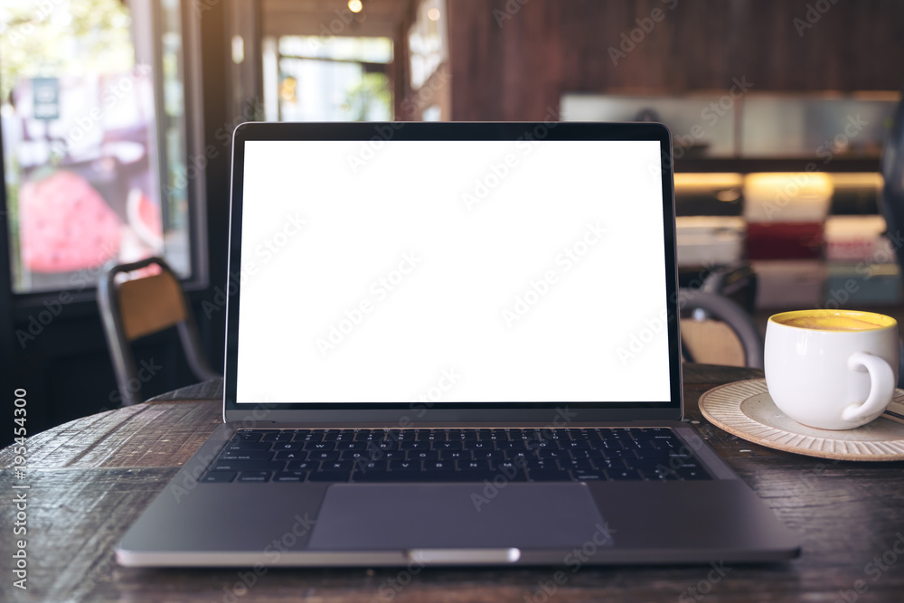 Mockup image of laptop with blank white desktop screen and coffee cup on wooden table in modern cafe Mockup image of laptop with blank white desktop screen and coffee cup on wooden table in modern cafe