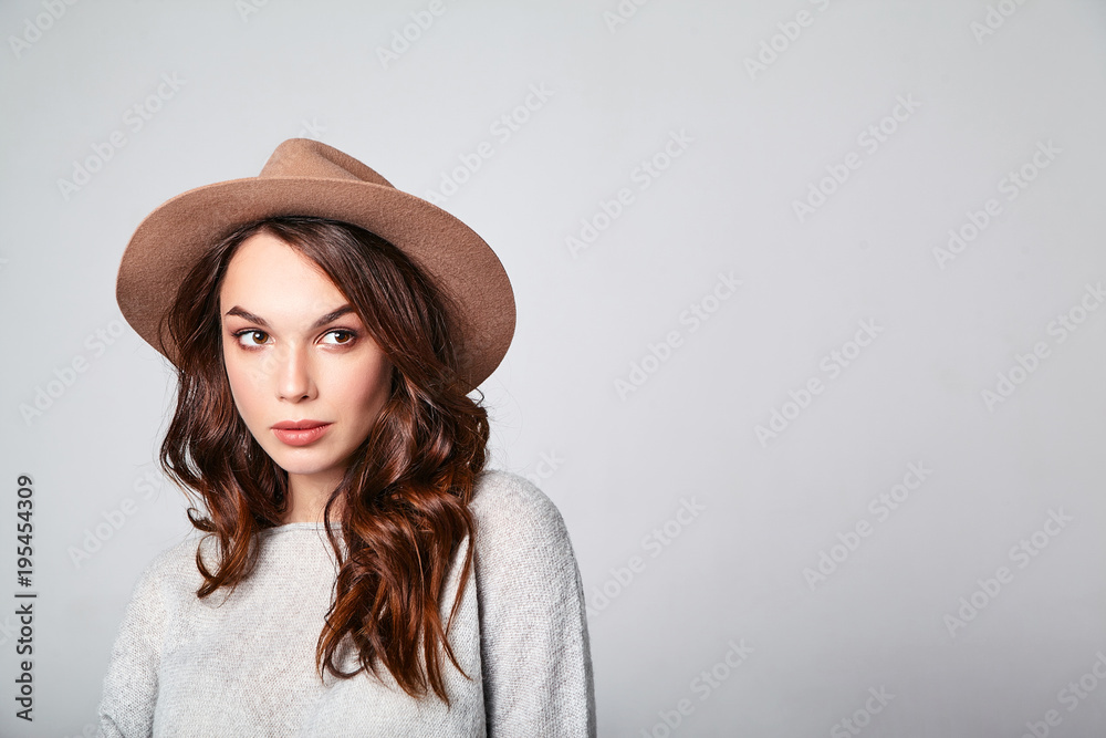 Portrait of young stylish laughing girl model in gray casual summer clothes in brown hat with natural makeup isolated on gray background. Looking at camera Portrait of young stylish laughing girl model in gray casual summer clothes in brown hat with natural makeup isolated on gray background. Looking at camera