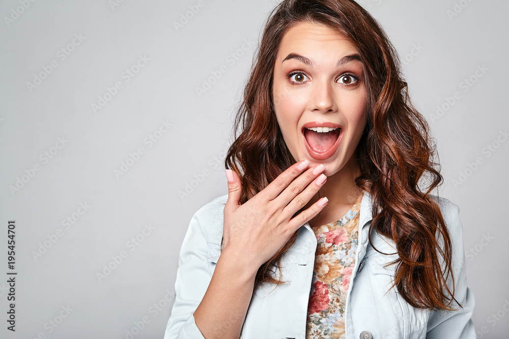 Portrait of young stylish laughing girl model in colorful casual summer clothes with natural makeup isolated on gray background. Looking at camera with hands near mouth