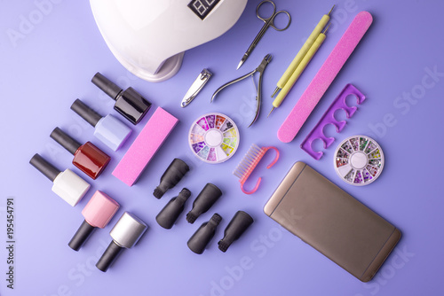 Set of cosmetic tools for manicure and pedicure on a purple background. Gel polishes, nail files and clippers, top view