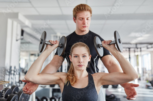 Trainer hilft junger Frau beim Hanteltraining photo