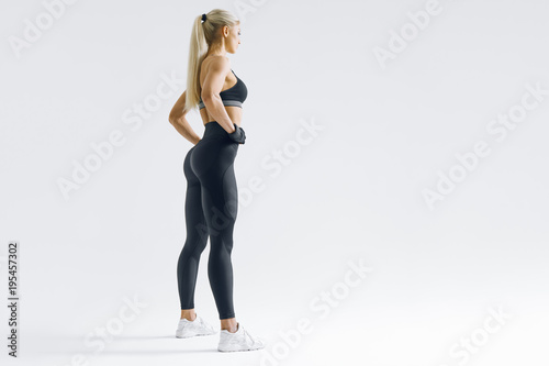 Full length portrait of fitness woman standing with her arms on hips Female model in sportswear over white background