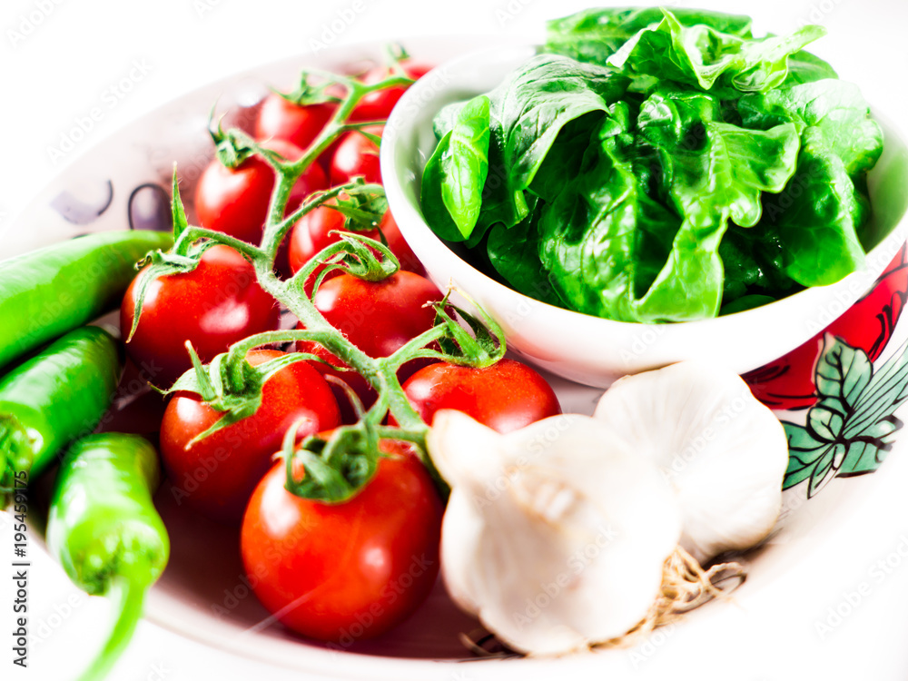 Little branch of cherry tomatoes, bowl of spinach, green hot peppers and garlic in plate over white isolated background. Little branch of cherry tomatoes, bowl of spinach, green hot peppers and garlic in plate over white isolated background.