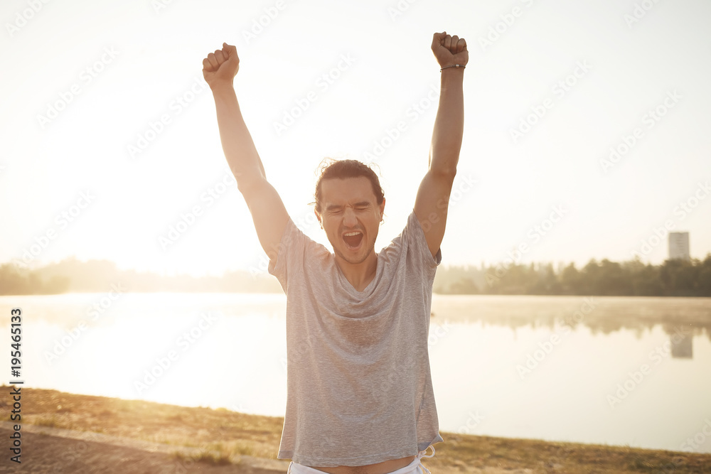 Sweaty man with raised hands happy to finish workout on sunrise Sweaty man with raised hands happy to finish workout on sunrise