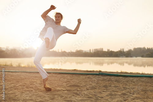 Athletic capoeira performer workout training on the beach sunris