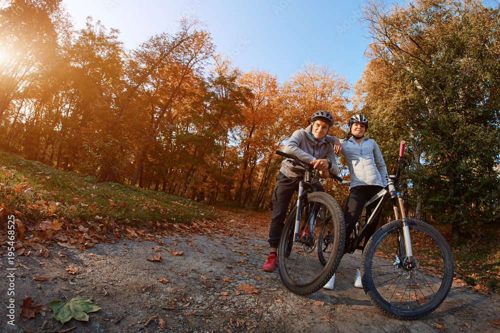 Fototapeta premium Happy young couple going for a bike ride on an autumn day in the park, backlight.