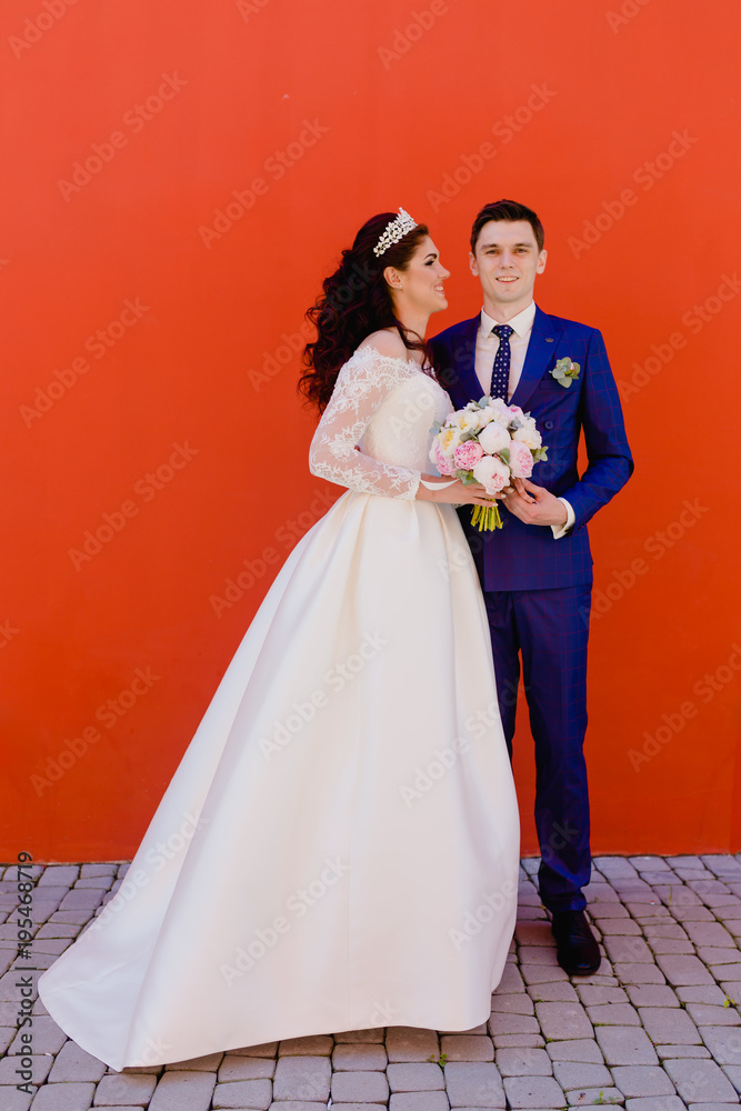 Beautiful couple newlyweds near the red wall