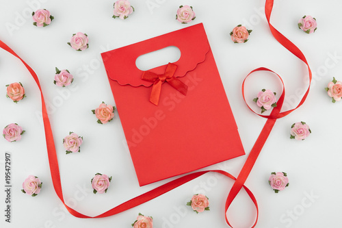 Red gift bag with pink and orange paper flowers with red ribbon on white background