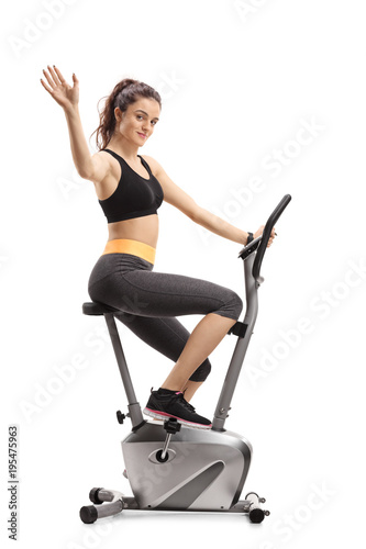Fitness woman working out on an exercise bike and waving at the camera