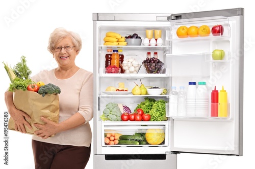 Mature woman holding a bag of groceries leaning against a refrigerator