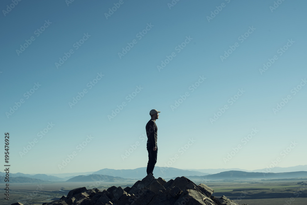 Retrato de hombre a contraluz en la cima de una montaña rocosa. Cielo azul al atardecer.