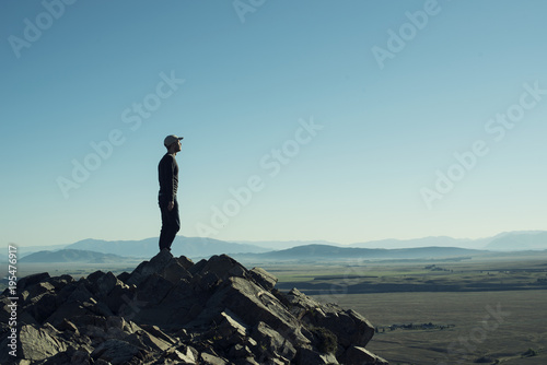 Retrato de hombre a contraluz en la cima de una montaña rocosa. Cielo azul al atardecer. photo