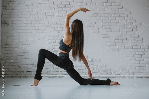 Slim woman practices yoga in white backlit studio