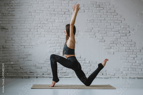 Slim woman practices yoga in white backlit studio