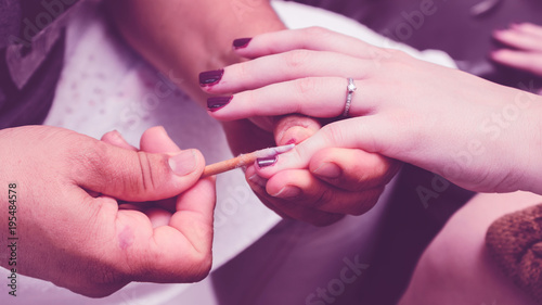 Manicurist removing the excess of ink from the polish nails after painting using a wooden stick with cotton on tip. Purple nail polish painting procedure. Close up on hands.