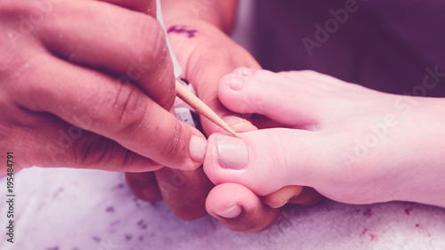 Manicurist removing the excess of ink from the polish nails from client feet after painting using a wooden stick. 